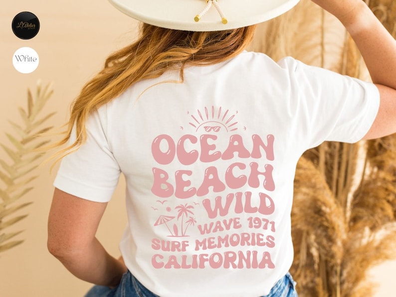 May include: White t-shirt with a pink graphic design that says "Ocean Beach Wild Wave 1971 Surf Memories California".