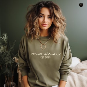 a woman sitting on a bed wearing a green sweatshirt