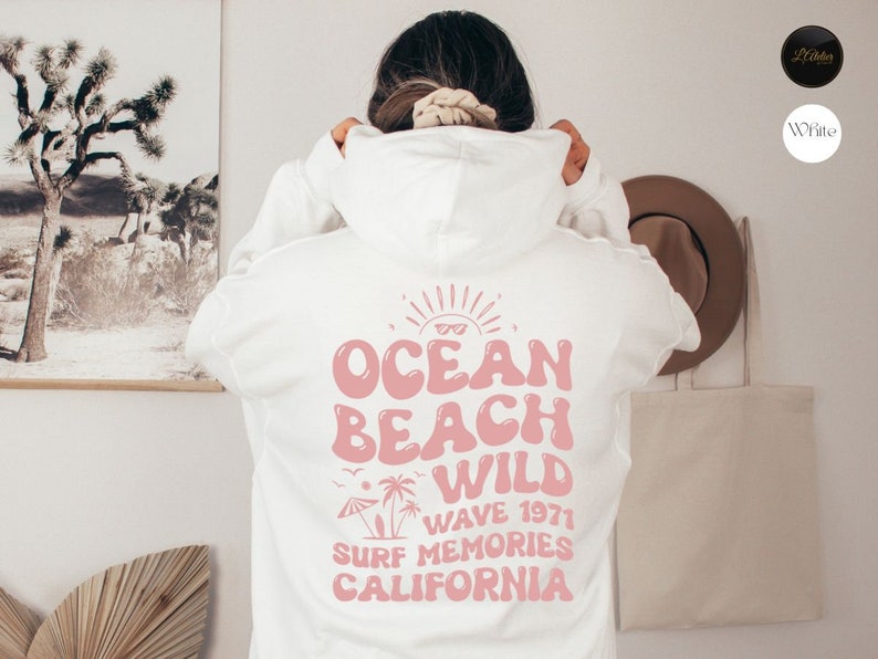 May include: White hoodie with a pink graphic print on the back that says "Ocean Beach Wild Wave 1971 Surf Memories California".