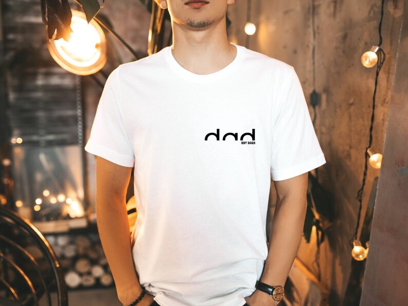 May include: White t-shirt with a black graphic that says "dad est. 2023".
