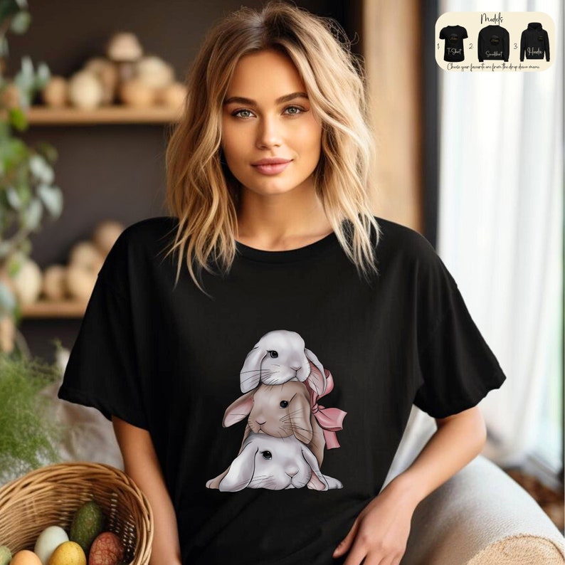 May include: A black t-shirt with a graphic of three stacked bunnies. The bunnies are white with pink noses and brown eyes. The top bunny has a pink bow.