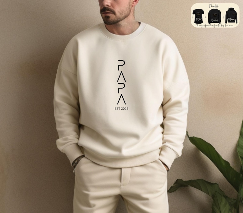 May include: A cream colored sweatshirt with a vertical black graphic that reads "PAPA EST 2025".