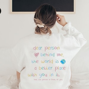May include: White sweatshirt with a colorful message that reads "dear person behind me, the world is a better place with you in it. love, the person in front of you".