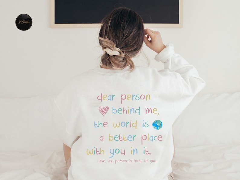 May include: White sweatshirt with a colorful message that reads "dear person behind me, the world is a better place with you in it. love, the person in front of you".
