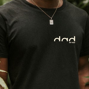 May include: A black t-shirt with a white logo that says "dad est 2023".