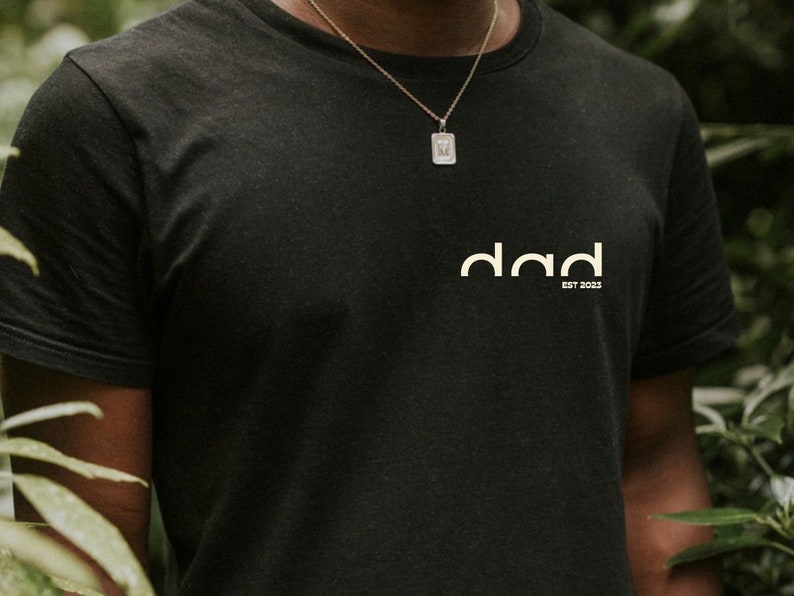 May include: A black t-shirt with a white logo that says "dad est 2023".