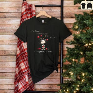 May include: Black t-shirt with a Christmas cat graphic. The cat is wearing reindeer antlers and holding ornaments. Text on the shirt reads "it's fine. I'm fine. everything's fine."