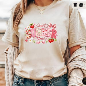 Könnte beinhalten: Beiges T-Shirt mit dem Schriftzug "Sweet Summer Time" in Rosa und Rot. Das Design beinhaltet Erdbeeren, Schleifen und florale Elemente. Das T-Shirt hat kurze Ärmel und eine lockere Passform.