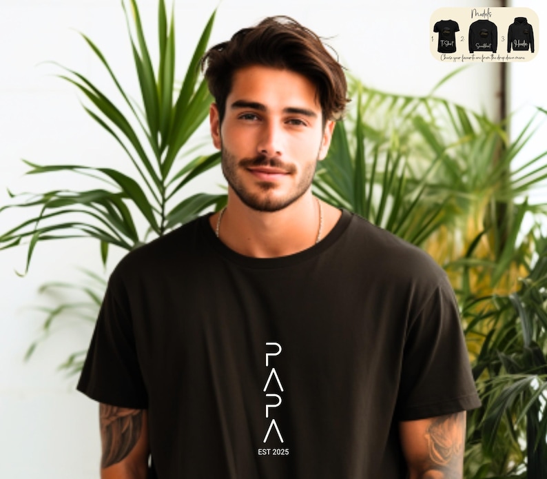 May include: A man wearing a black t-shirt with a white graphic design that says "PAPA EST 2025".
