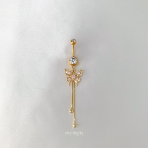 May include: Gold-colored belly button ring featuring a butterfly design with clear, sparkling accents. The butterfly has dangling chains with small, round embellishments. The text "dry digits" is at the bottom.
