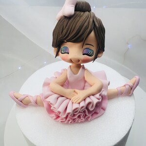 Puede incluir: Un adorno de pastel de bailarina de fondant rosa y marr&oacute;n con un lazo rosa en el pelo. Lleva un tut&uacute; rosa y zapatillas de ballet rosas.