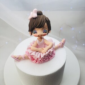 Puede incluir: Un pastel blanco con una figurita de bailarina de fondant en la parte superior. La bailarina lleva un tut&uacute; rosa y tiene el pelo casta&ntilde;o con un lazo rosa.