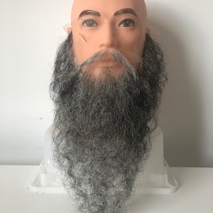 May include: A mannequin head with a long, gray and black beard. The beard is styled in a long, flowing style.