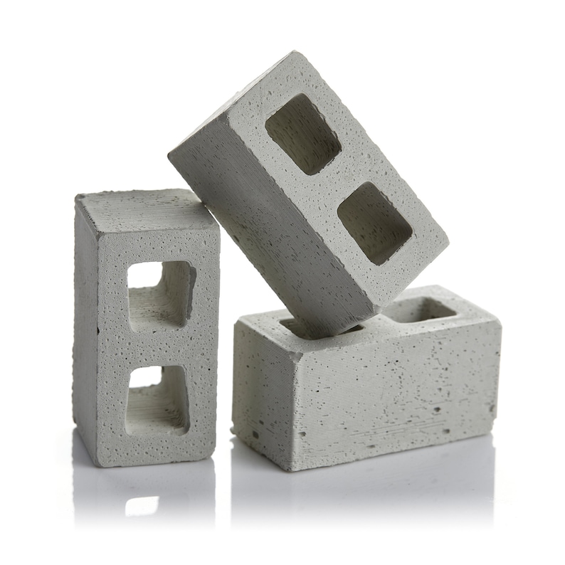 May include: Three grey concrete cinder blocks stacked on top of each other. The top block is lying on its side.