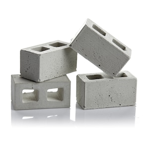 May include: Four grey concrete cinder blocks stacked in a pyramid shape. The blocks have two rectangular holes in the centre.