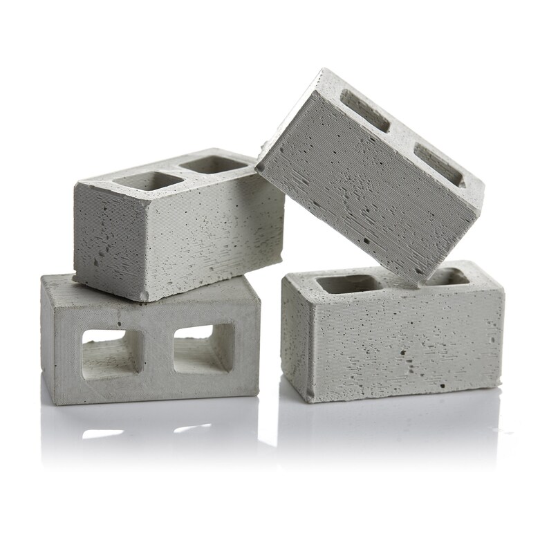 May include: Four grey concrete cinder blocks stacked in a pyramid shape. The blocks have two rectangular holes in the centre.