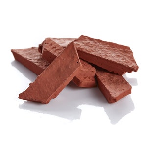 May include: A collection of reddish-brown, rectangular bricks with textured surfaces and irregular edges. The bricks are stacked and arranged, showcasing their rough, uneven texture. The image is set against a white background, highlighting the color and form of the bricks.