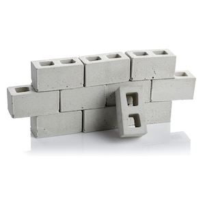 May include: A wall made of grey concrete cinder blocks. The blocks are arranged in a staggered pattern, with one block partially overlapping the others. The blocks have two holes in each.