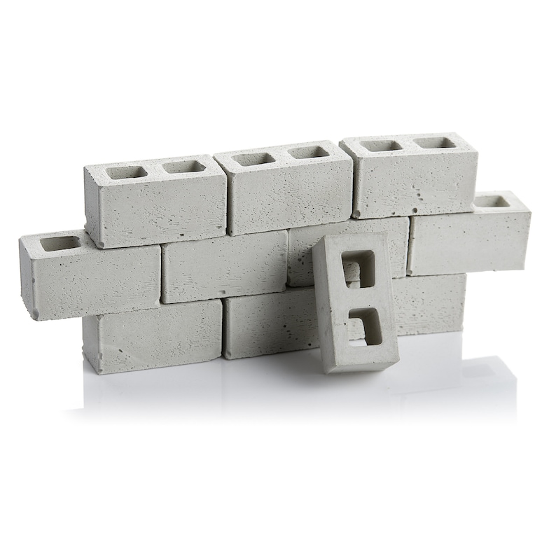 May include: A wall made of grey concrete cinder blocks. The blocks are arranged in a staggered pattern, with one block partially overlapping the others. The blocks have two holes in each.