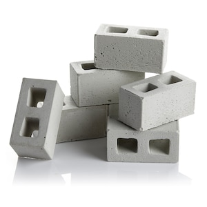 May include: A stack of six grey concrete breeze blocks, each with two rectangular holes. The blocks are arranged in a pyramid shape.