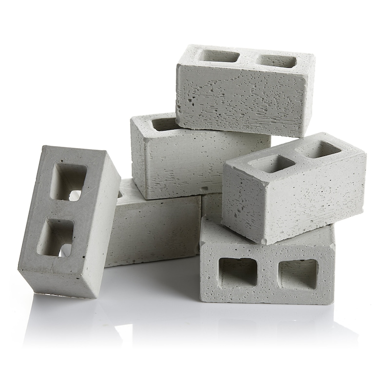 May include: A stack of six grey concrete breeze blocks, each with two rectangular holes. The blocks are arranged in a pyramid shape.