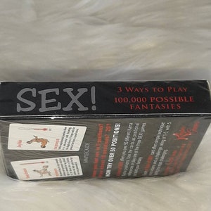 May include: A black box with the word "SEX!" in large white letters. The box also has the text "3 WAYS TO PLAY" and "100,000 POSSIBLE FANTASIES". Sample cards are visible, along with the text "NOW TRY OVER 50 POSITIONS!"