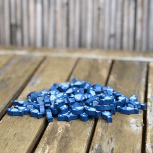 May include: A pile of blue wooden game pieces shaped like fish with white designs. The pieces are on a wooden surface.