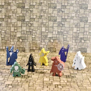 May include: A selection of brightly coloured wooden game pieces, featuring figures in blue, yellow, green, black, red, and white. The pieces are designed as various characters, such as wizards and warriors, and are arranged on a stone-like surface.