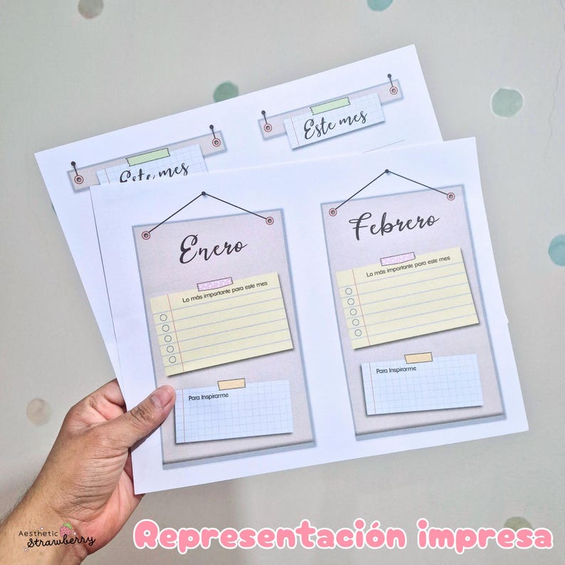May include: Two printed sheets featuring monthly planner templates. Each sheet displays hanging rectangular panels labeled Enero and Febrero, with yellow lined checklists titled Lo m&aacute;s importante para este mes and blue grid notes labeled Para inspirarme.