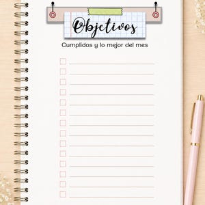 May include: A spiral-bound notebook with white pages featuring a grid-patterned header that reads "Objetivos" and the text "Cumplidos y lo mejor del mes" below it. The page includes a checklist with fifteen horizontal lines and empty square boxes.
