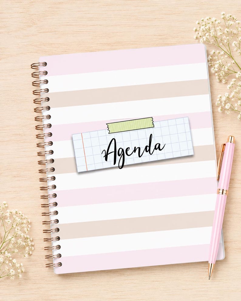 May include: A spiral-bound agenda notebook featuring horizontal stripes in alternating shades of light pink and beige. A rectangular piece of grid paper with the word Agenda written in black script is attached to the center with green tape.
