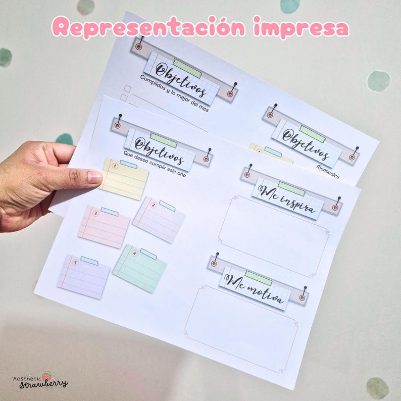 May include: A printed planner page featuring sections labeled Objetivos, Me inspira, and Me motiva. The layout includes pastel-colored index cards numbered one through six, decorative headers with pushpin graphics, and lined writing spaces.