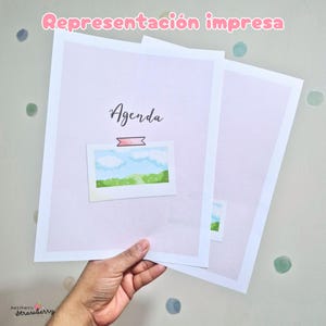 May include: Two printed sheets of paper with a light lavender background. The top sheet features the word Agenda in black script, a pink rectangular graphic, and a small illustration of a blue sky with white clouds over a green landscape.