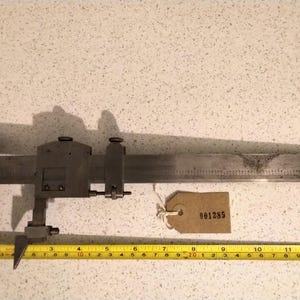 May include: A silver metal measuring tool with a ruler and a sliding caliper. The tool has a tag attached with the number 001285.