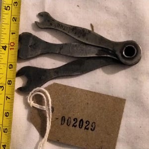 May include: A set of three vintage metal wrenches with a tag that reads "002029" and a yellow ruler showing measurements in inches. The wrenches are dark gray and appear to be well-used. The ruler is marked with black numbers.
