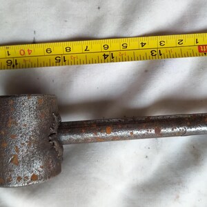 Peut inclure: Un outil en m&eacute;tal rouill&eacute; avec une t&ecirc;te cylindrique et une longue poign&eacute;e. Un ruban &agrave; mesurer jaune est plac&eacute; &agrave; c&ocirc;t&eacute; de l'outil, indiquant des mesures. L'outil mesure environ 35,5 cm de long.