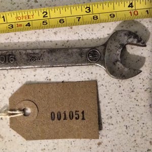 May include: A silver wrench with the text "01A17016 Ford" on the handle. A brown tag with the number "001051" is attached to the wrench.