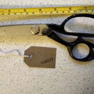May include: A pair of black handled fabric shears with a silver blade and a brown tag with the number 300657 printed on it.