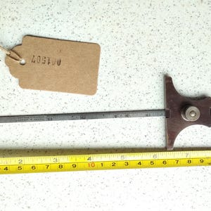 May include: A vintage wooden and metal protractor with a ruler marked in inches. The protractor is brown and has a metal ruler with markings up to 6 inches. A yellow tape measure is also visible in the image, marked in inches.