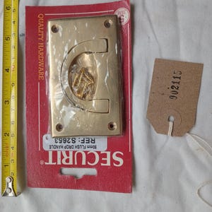 May include: A brass-coloured 90mm flush drop handle, packaged on a red card with the brand name SECURIT. The card also displays the text "QUALITY HARDWARE" and the reference number S2653. A small tag with the number 002115 is attached.