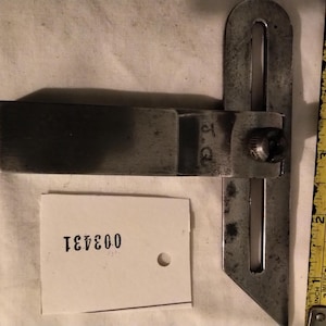May include: A vintage metal T-bevel tool with a locking screw and the initials J.G. engraved on the blade. A yellow measuring tape shows the tool is approximately 12.7 cm long. A white tag with the black printed number 003431 is included.