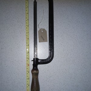 May include: A black metal saw with a wooden handle and a tag with the number 000644. The saw is approximately 43 cm long.