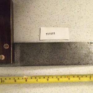 May include: A metal try square with a wooden handle. The handle has three brass screws. The try square is 28 cm long. The number 600044 is written on a white piece of paper.