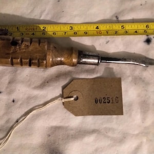 May include: A vintage wood-handled tool with a curved metal blade, approximately 6 inches long, is shown with a yellow measuring tape. A brown tag with the number "002516" is attached.