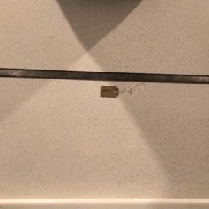May include: A long, thin, dark grey metal bar with a small brown tag attached to it. The tag has the word "SMALL" written on it.