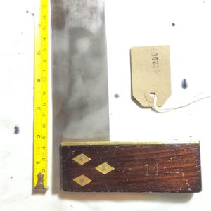 May include: A vintage marking gauge with a steel blade and a wooden handle. The handle is dark brown with brass accents and the number "14" is visible. A measuring tape is next to the gauge. The blade is approximately 12 cm long.