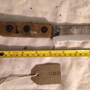 May include: A vintage knife with a wooden handle and a metal blade, approximately 8 inches long. A yellow tape measure is placed next to the knife. A small tag with the number "002533" is also present.