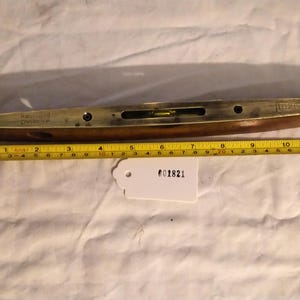 Puede incluir: Un nivel antiguo de latón y madera con una ampolla de burbujas transparente. El nivel mide aproximadamente 30 cm de largo. El texto "Robert Sorby, Sheffield, England" es visible. Una cinta métrica amarilla se coloca junto al nivel.