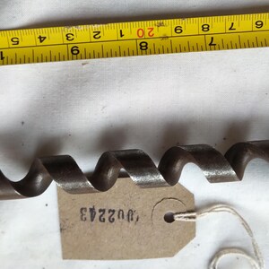 Peut inclure: Une m&egrave;che de tari&egrave;re ancienne en m&eacute;tal fonc&eacute; avec un design en spirale. Un ruban &agrave; mesurer jaune avec des marquages noirs est en arri&egrave;re-plan. Une petite &eacute;tiquette avec le num&eacute;ro "U02243" est attach&eacute;e &agrave; la m&egrave;che.