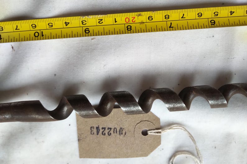 Peut inclure: Une m&egrave;che de tari&egrave;re ancienne en m&eacute;tal fonc&eacute; avec un design en spirale. Un ruban &agrave; mesurer jaune avec des marquages noirs est en arri&egrave;re-plan. Une petite &eacute;tiquette avec le num&eacute;ro "U02243" est attach&eacute;e &agrave; la m&egrave;che.